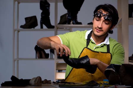Young shoemaker in workshop at nightの写真素材