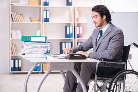 Young handsome employee in wheelchair at the officeの写真素材