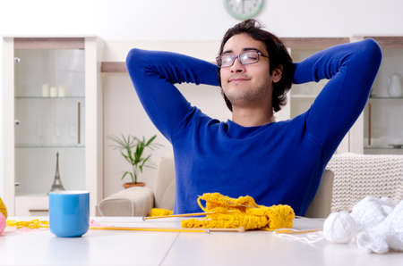 Young good looking man knitting at home