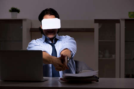 Young employee with virtual glasses at night in the office
