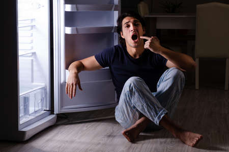 Man breaking diet at night near fridgeの写真素材