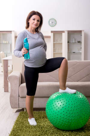 Aged pregnant woman doing exercises at homeの写真素材