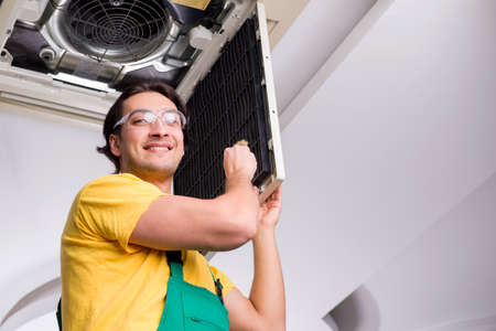 Young repairman repairing ceiling air conditioning unitの写真素材
