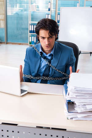 Chained male employee unhappy with excessive workの写真素材