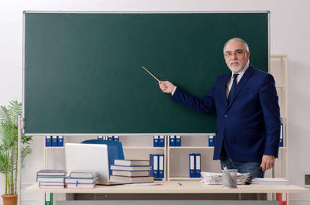 Aged male teacher in front of chalkboard