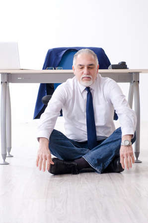 Aged businessman doing yoga exercises in the officeの写真素材