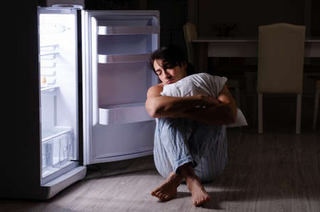 Man breaking diet at night near fridgeの写真素材