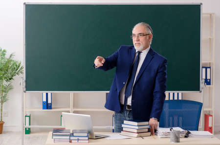 Aged male teacher in front of chalkboard