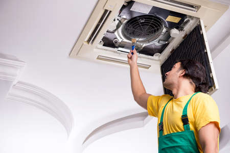 Young repairman repairing ceiling air conditioning unitの写真素材