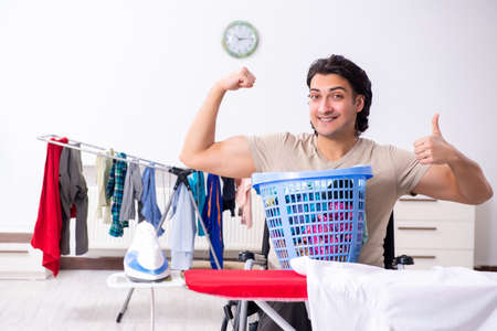 Young man in wheel-chair doing ironing at homeの写真素材