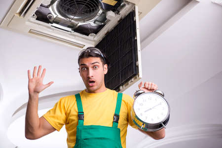 Young repairman repairing ceiling air conditioning unitの写真素材