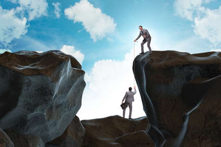 Businessman helping colleague with ropeの写真素材