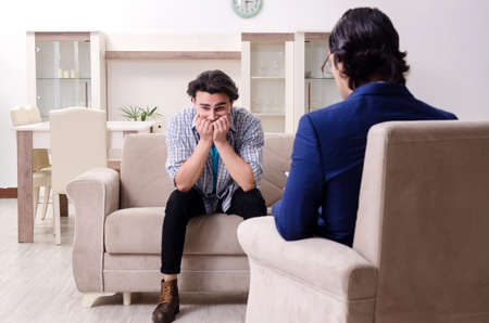 Young male patient discussing with psychologist personal problemの写真素材