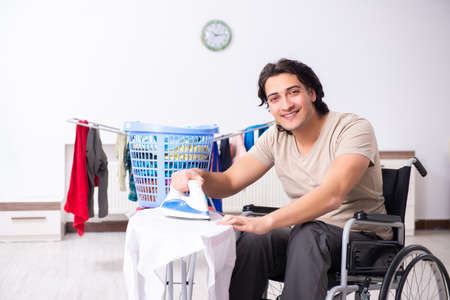 Young man in wheel-chair doing ironing at homeの写真素材