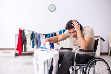 Young man in wheel-chair doing ironing at homeの写真素材