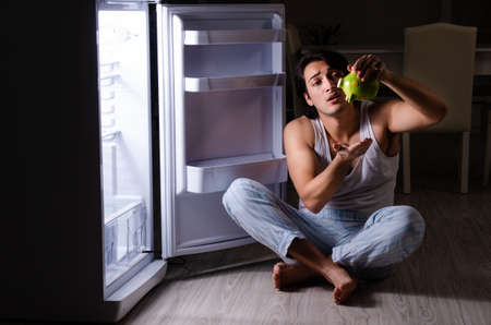 Man breaking diet at night near fridgeの写真素材