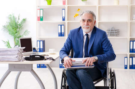 Aged employee in wheelchair working in the officeの写真素材