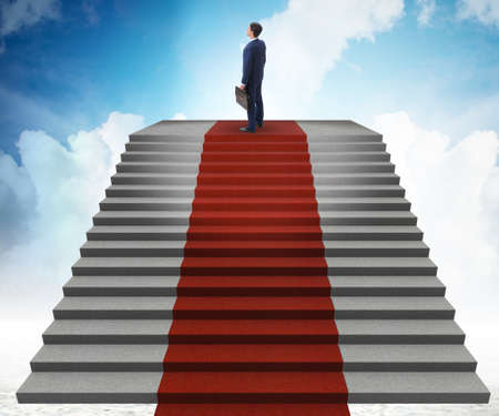 Young businessman climbing stairs and red carpet into skyの写真素材