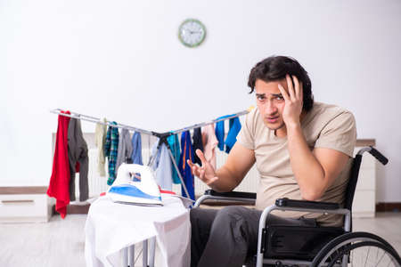 Young man in wheel-chair doing ironing at homeの写真素材