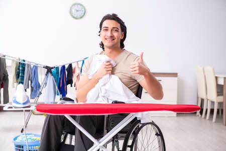 Young man in wheel-chair doing ironing at homeの写真素材