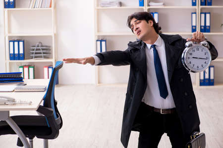 Young male employee in the office in time management conceptの写真素材