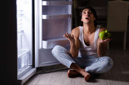 Man breaking diet at night near fridgeの写真素材