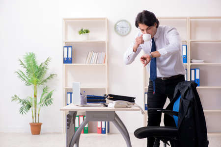 Young male employee in the office in time management conceptの写真素材