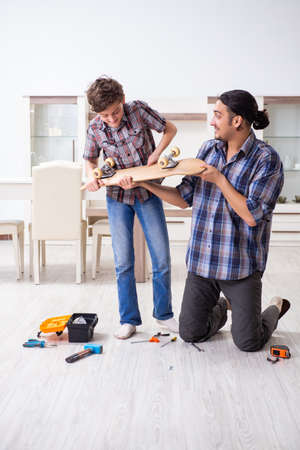 Young father repairing skateboard with his son at homeの写真素材