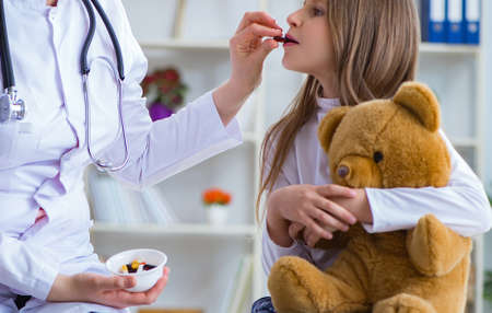 Woman female doctor examining little cute girl with toy bearの写真素材