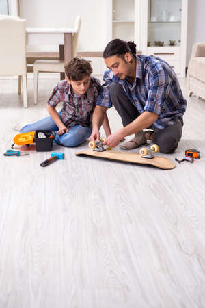 Young father repairing skateboard with his son at homeの写真素材