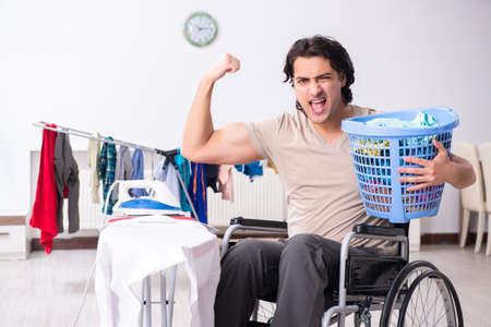 Young man in wheel-chair doing ironing at homeの写真素材