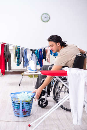 Young man in wheel-chair doing ironing at homeの写真素材