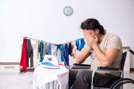 Young man in wheel-chair doing ironing at homeの写真素材