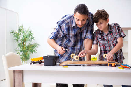 Young father repairing skateboard with his son at homeの写真素材