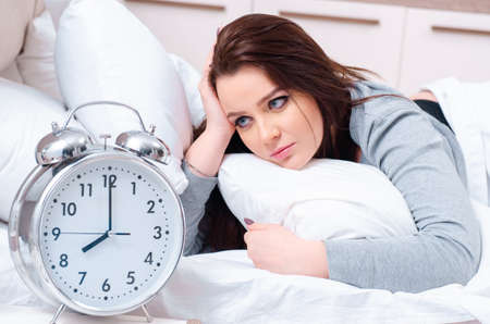 Young woman lying on the bed in time management conceptの写真素材