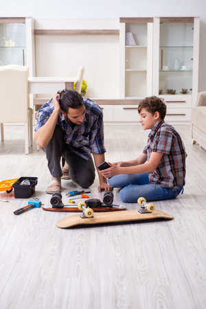 Young father repairing skateboard with his son at homeの写真素材
