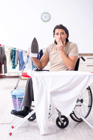 Young man in wheel-chair doing ironing at homeの写真素材