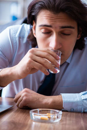 Male employee drinking vodka and smoking cigarettes at workplaceの写真素材