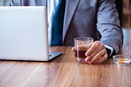 The male employee drinking alcohol and smoking cigarettes at workplaの写真素材