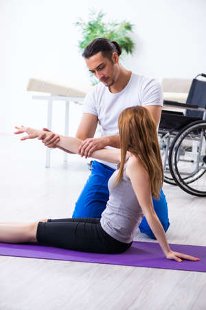 Male physiotherapist doing exercises with injured woman on floorの写真素材
