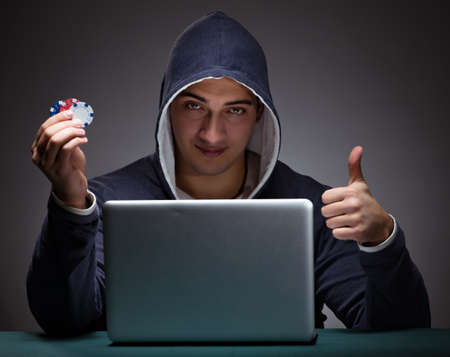 Young man wearing a hoodie sitting in front of a laptop computerの写真素材