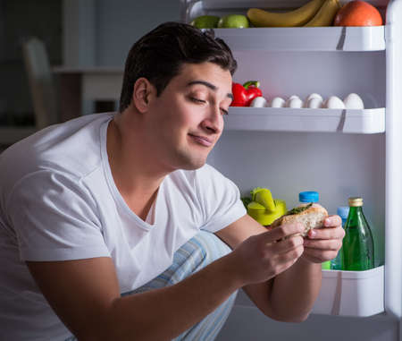 Man at the fridge eating at nightの写真素材