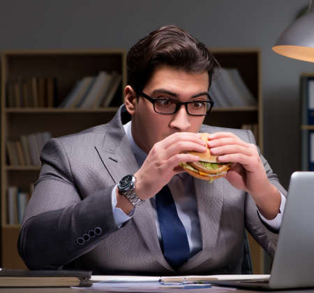 Businessman late at night eating a burgerの写真素材