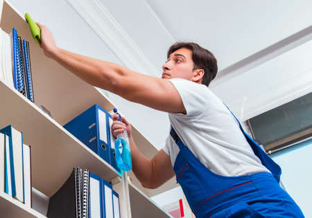 Male office cleaner cleaning shelves in office