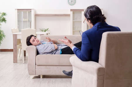Young male patient discussing with psychologist personal problemの写真素材