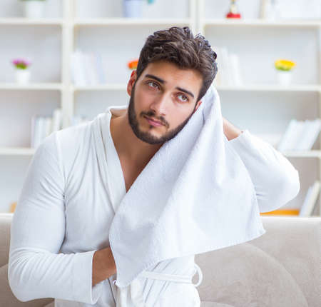 Young man in a bathrobe after shower drying hair with a towelの写真素材
