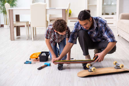 Young father repairing skateboard with his son at homeの写真素材