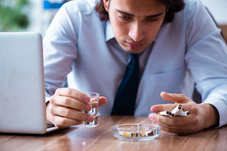 Male employee drinking vodka and smoking cigarettes at workplaceの写真素材