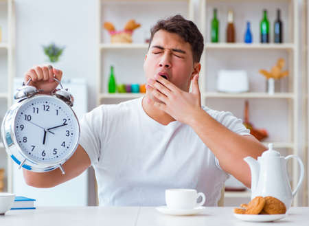 Man with alarm clock falling asleep at breakfastの写真素材