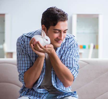Young man playing with pet rabbit at homeの写真素材